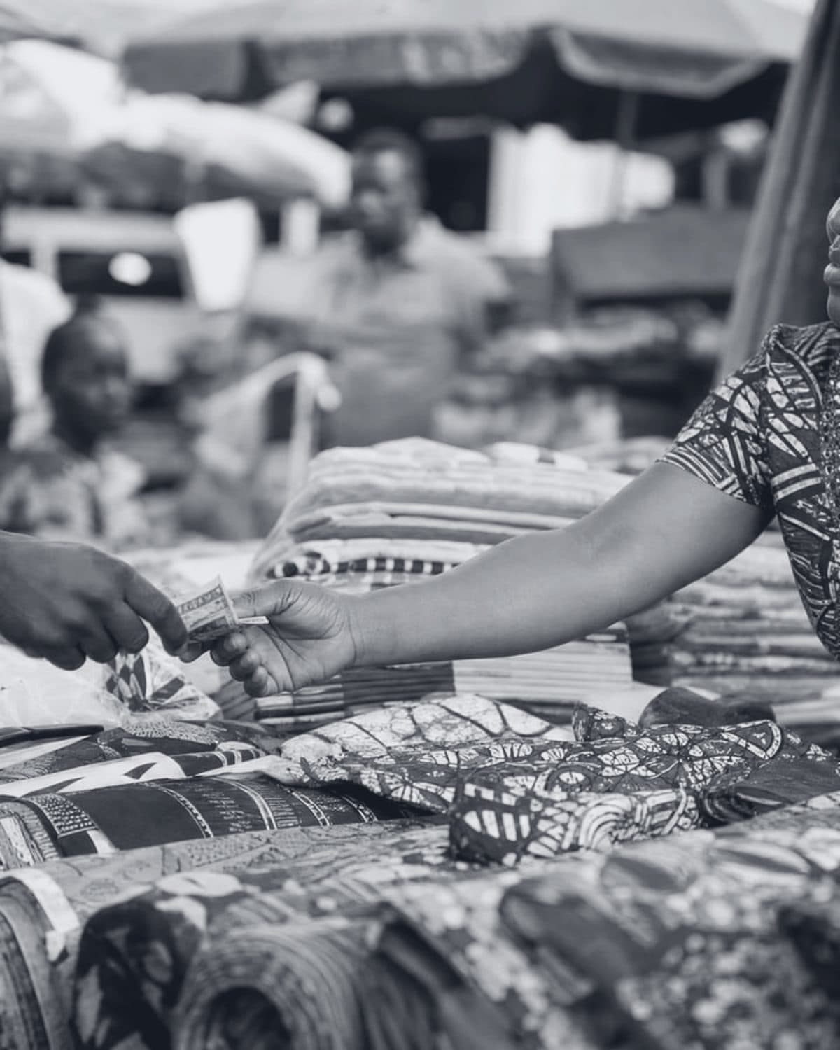 An African market trader receiving payment at her fabric stall.