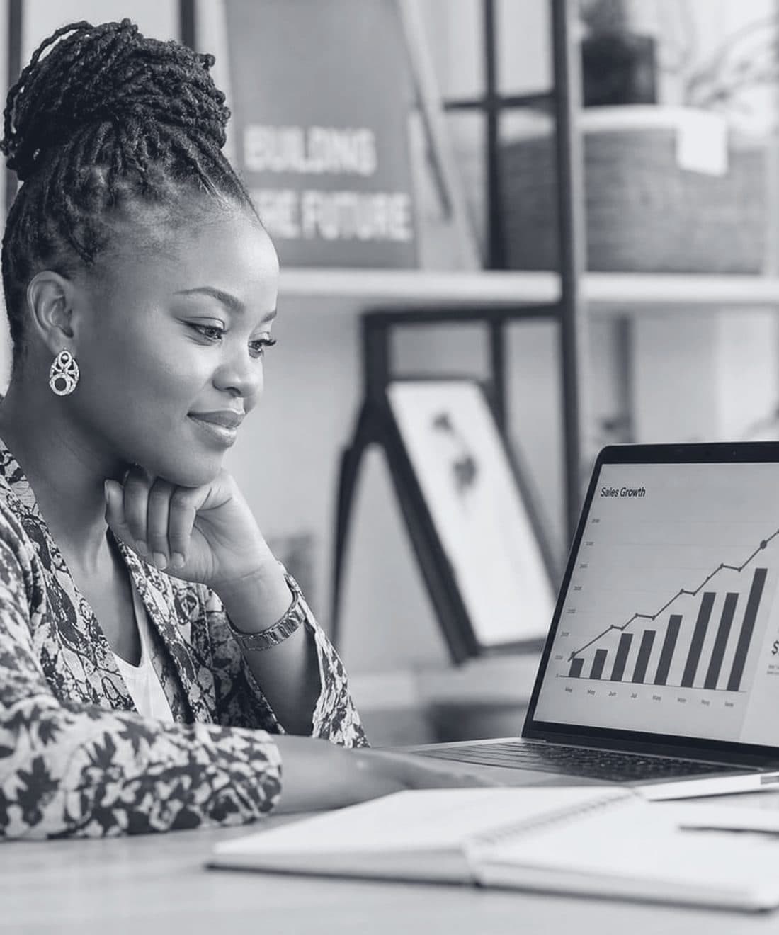 An African founder at her desk reviewing a rising sales growth chart on her laptop.
