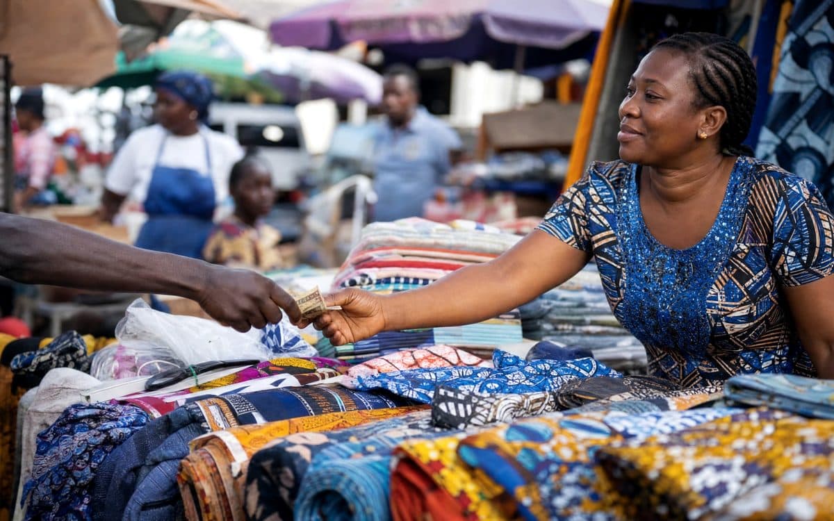 An African market trader receiving payment at her fabric stall.